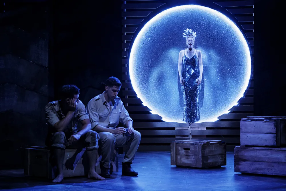 Two soldiers on stage in Yank!, a woman in a sequinned gown silhouetted against a lit moon behind them